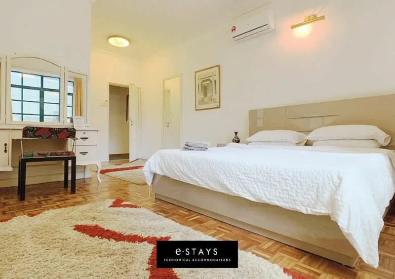 Bedroom features: queen-size bed with white bedding, wooden parquet flooring, white painted walls, ceiling light fixture, wall-mounted split AC unit, large window with grid pattern, dressing table with mirror, decorative area rug with geometric pattern, bedside table, framed artwork on wall; style: modern.