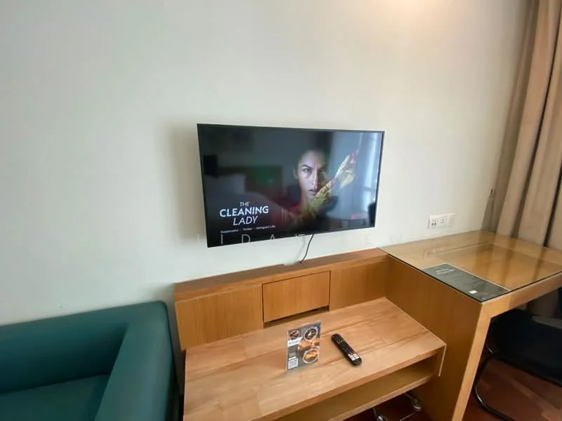 Living features: green fabric sofa, wall-mounted flat-screen TV, wooden TV console, glass-top side table, remote control, decorative brochure on table, light-colored painted walls, curtains; style: modern.