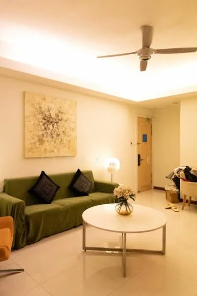 Living features: green fabric sofa, white round coffee table, 5-blade ceiling fan with light, framed artwork on wall, laminate flooring, wall-mounted light, decorative vase with flowers, two black throw pillows, orange accent chair, door leading to hallway; style: modern.