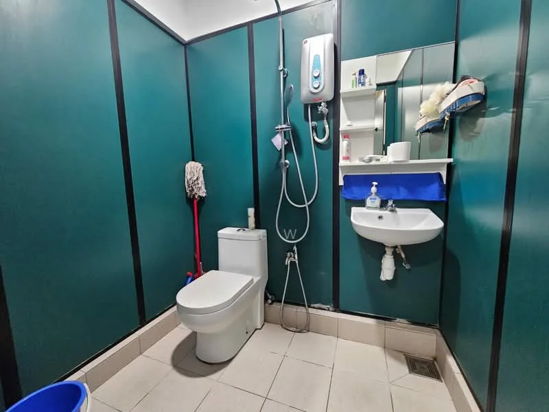 Bathroom features: green painted walls, white ceramic floor tiles, one-piece toilet, wall-mounted basin, chrome basin mixer faucet, shower with handheld showerhead, shower hose, mirror above basin, shelf for toiletries, mop, cleaning bucket.