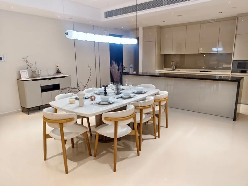 Dining features: round dining table, 8 upholstered dining chairs with wooden legs, white tableware, decorative centerpiece with branches, pendant light fixture with multiple bulbs, cream painted walls, glossy cabinetry, black countertop, built-in kitchen appliances visible in background, open-plan layout with kitchen, light-colored flooring; style: modern.