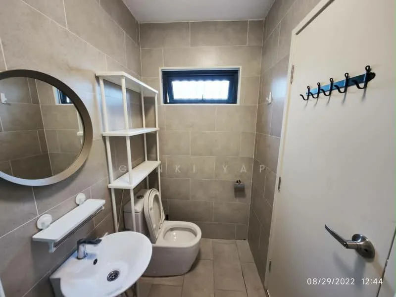 Bathroom features: grey tiled walls, light grey tiled flooring, round mirror, white wall-mounted sink, chrome faucet, toilet, white shelving unit, window with horizontal bars, towel hook on door; style: modern.