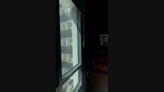 Room features: large floor-to-ceiling windows, black walls, dark flooring, visible balcony railing, interior view of adjacent building, minimalist decor, sofa visible in the background; style: modern.