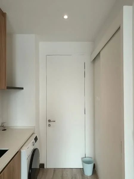 Room features: white walls, light wood cabinetry, white countertop, built-in washing machine, single white door, sliding door, recessed ceiling light, laminate flooring; style: modern.