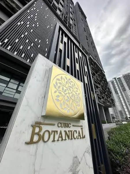 Exterior type: high-rise condominium; features: modern facade with decorative elements, golden signage with logo, glass windows, concrete structure, landscaped greenery at base, multiple storeys visible, architectural detailing on facade; style: contemporary.