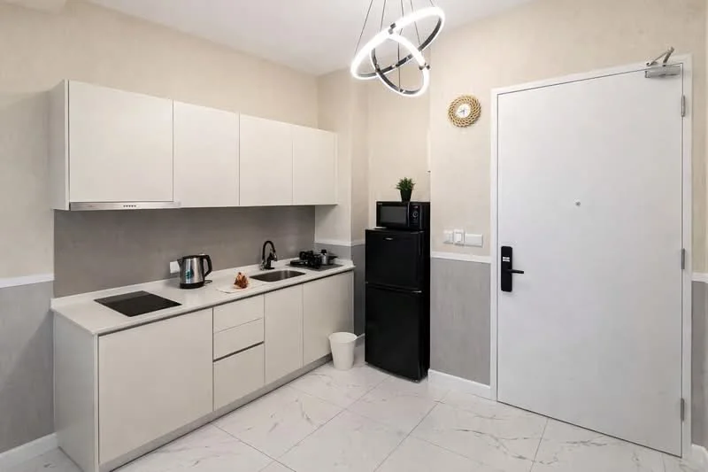 Kitchen features: white cabinetry, black refrigerator, built-in oven, electric cooktop, kettle, black sink, chrome faucet, marble tile flooring, pendant light fixture, white walls with light grey accent, countertop with integrated backsplash, waste bin; style: modern.