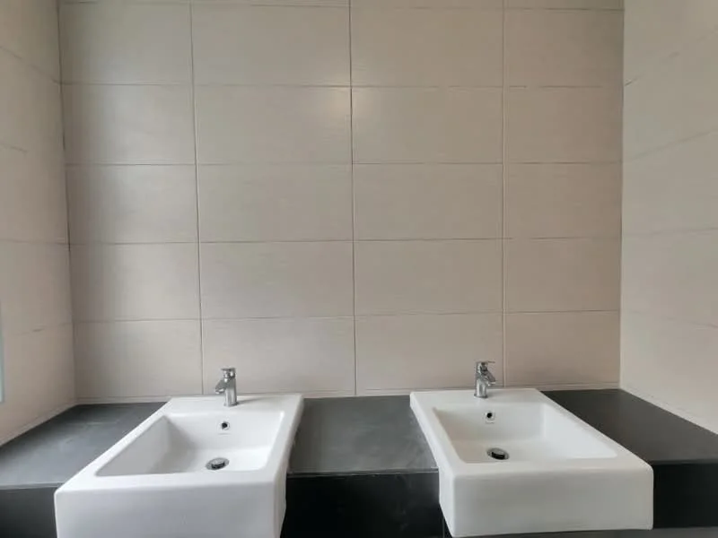 Bathroom features: double-sink vanity with white ceramic sinks, chrome basin mixers, black countertop, light beige tile walls, large format tiles, minimalist design; style: modern.