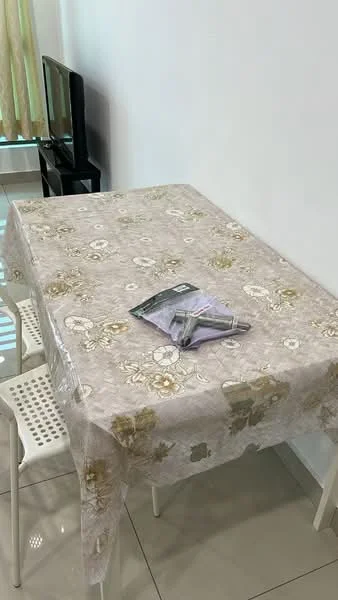 Dining features: rectangular dining table, tablecloth with floral pattern, four white plastic chairs, ceramic tile flooring, white painted walls, natural light from window, TV console in background; style: modern.