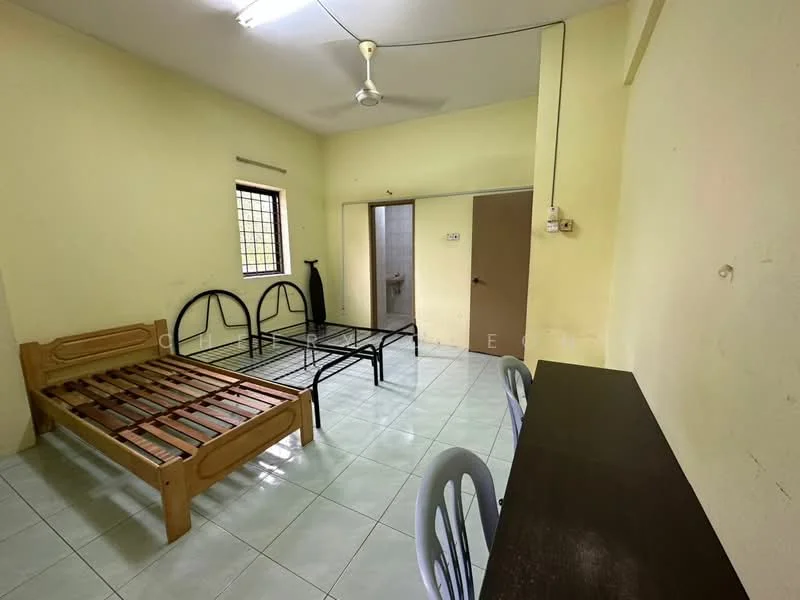 Room features: yellow painted walls, white tiled flooring, ceiling fan, single bed frame, metal bed frame, wooden dining table, plastic dining chairs, window with metal grille, doorway leading to bathroom, light fixture on ceiling; style: minimalist.