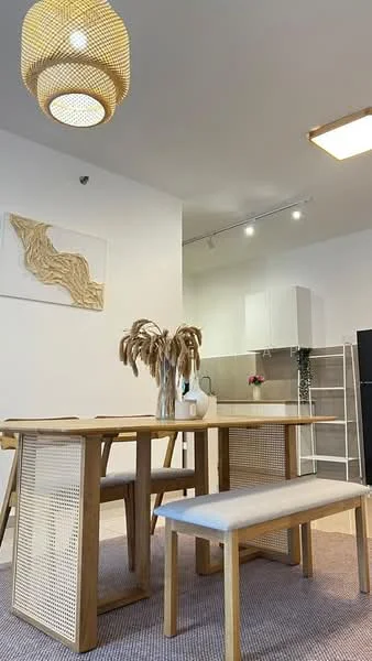 Dining features: wooden dining table, upholstered bench seating, woven pendant light, white walls, light grey flooring, decorative wall art, kitchen cabinetry in white, kitchen backsplash in grey tiles, floor-to-ceiling windows, vase with dried flowers; style: modern.