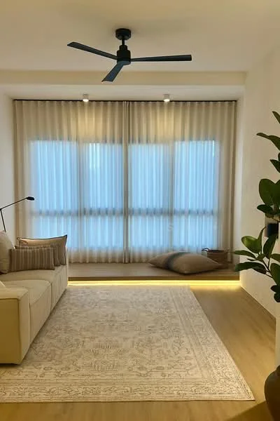 Living features: 3-seater fabric sofa in beige, floor-to-ceiling windows, sheer curtains, wooden flooring, area rug with intricate pattern, ceiling fan with light, decorative plant, soft cushions, LED strip lighting along the base, neutral wall color; style: modern; view: city.