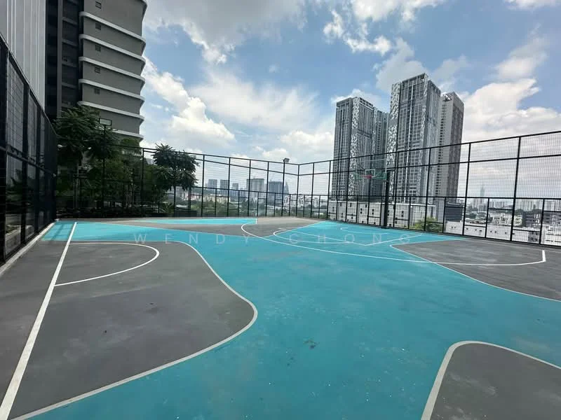 Exterior type: basketball court; features: outdoor basketball court, blue court surface, fenced perimeter, urban skyline view, surrounded by greenery, two basketball hoops; style: modern.