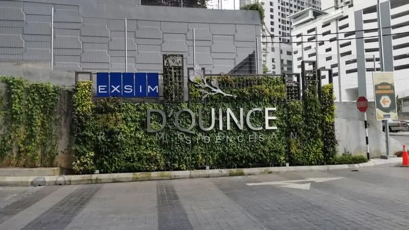 Exterior features: modern facade with greenery, metal gate, paved driveway, signage with name 'D QUINCE', surrounding urban environment, parking structure visible in background; style: modern.