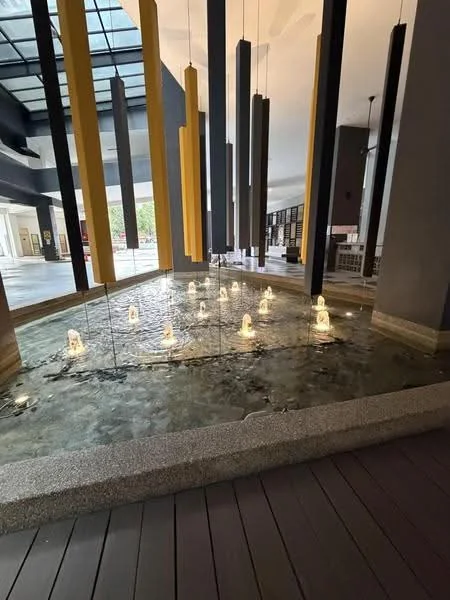 Exterior type: clubhouse; features: water feature with illuminated fountains, glass wall, hanging vertical elements in yellow and grey, wooden decking, open-air design, modern architectural elements; style: modern.