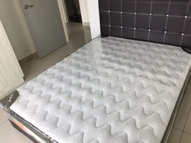 Room features: queen-size mattress, grey patterned mattress cover, brown upholstered headboard with button tufting, white walls, light-colored tiled flooring, door visible in background.