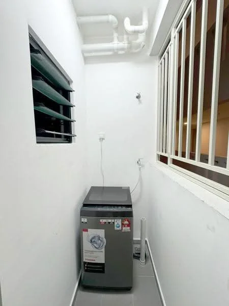 Laundry features: top-load washing machine in silver, white painted walls, grey tiled flooring, window with louvre panes, metal grille window, plumbing connections visible, drainage pipe, exposed piping.