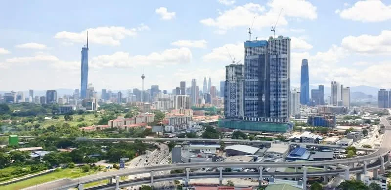 Exterior type: high-rise condominium; features: glass curtain wall, approximately 30-storey high-rise, surrounded by mature greenery, city skyline view, construction cranes visible, urban context with main road, adjacent to highway; style: modern.
