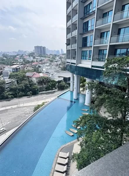 Exterior type: high-rise condominium; features: infinity pool, pool deck with loungers, glass curtain wall facade, balconies on upper floors, surrounded by greenery, city skyline view, manicured landscaping; style: modern.