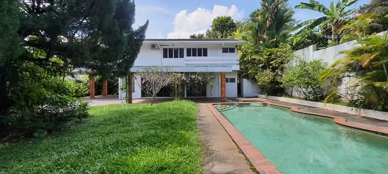 Exterior type: detached bungalow; features: swimming pool, manicured lawn, mature trees, tropical landscaping, brick pathway, covered car porch, large windows, garden area, fenced perimeter; style: modern.