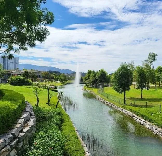 Exterior type: landscape garden; features: manicured lawn, mature trees, water fountain, serene waterway, stone-paved walkway, greenery, fenced area, mountain view in background, clear blue sky; style: modern.