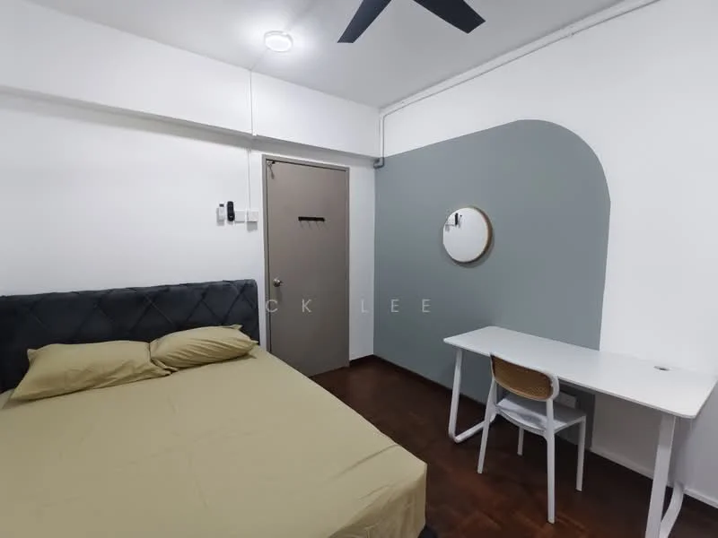 Bedroom features: queen-size bed with grey upholstered headboard, light brown bedding, white painted walls, grey accent wall, wooden flooring, ceiling fan, round wall mirror, study desk with white surface and wooden legs, white chair, door with simple handle; style: modern.