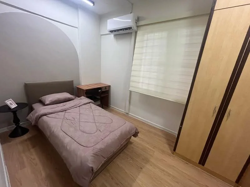 Bedroom features: single bed with beige bedding, wooden bedside table, black round side table, built-in wardrobe with wooden finish, window with sheer blinds, wall-mounted air conditioning unit, light-colored wooden flooring, neutral painted walls; style: modern.
