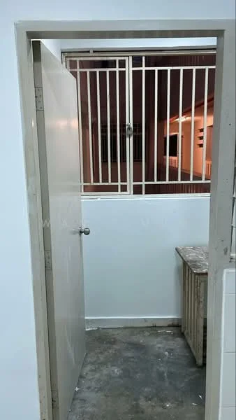 Room features: white painted walls, concrete flooring, metal security grille, wooden door, door handle, window with security bars.
