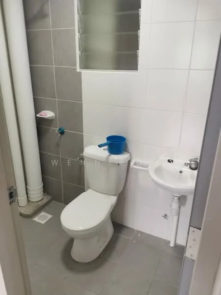 Bathroom features: white ceramic toilet, small sink with chrome faucet, grey tiled walls, white tiled walls, grey tile flooring, window for natural light, plumbing pipes visible, blue plastic bucket; style: modern.