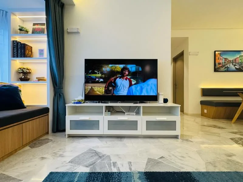 Living features: marble tile flooring, white painted walls, built-in shelving unit with decorative items, wall-mounted TV, TV console with grey and white drawers, sofa with cushions, curtains in blue, recessed LED lighting, decorative wall art, area rug with geometric pattern; style: modern.