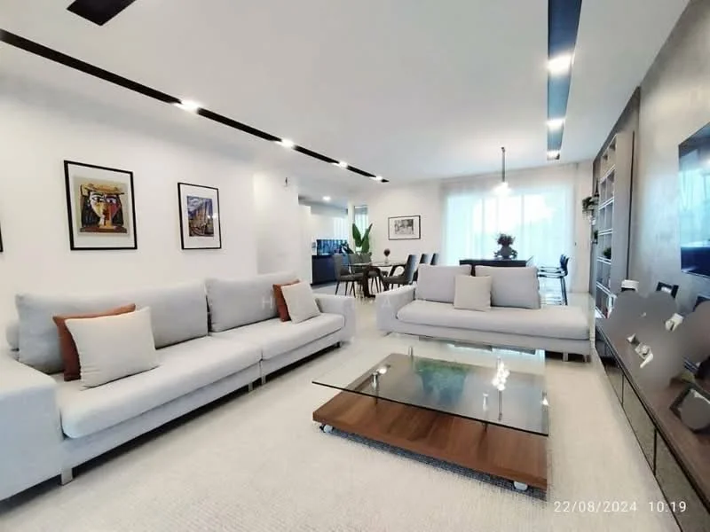 Living features: 2-seater fabric sofa in light grey, 3-seater fabric sofa in light grey, glass coffee table with wooden base, wall-mounted TV, built-in shelving unit, framed artwork on walls, recessed LED downlights, cream wall-to-wall carpet, floor-to-ceiling windows with sheer curtains, decorative indoor plant; style: modern.