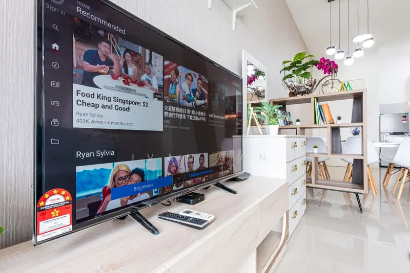 Living features: large flat-screen TV, TV console with storage, remote control, light-colored wooden cabinetry, white walls, glossy tile flooring, decorative plants, open shelving, dining area visible in background, natural light from windows, modern decor; style: modern.