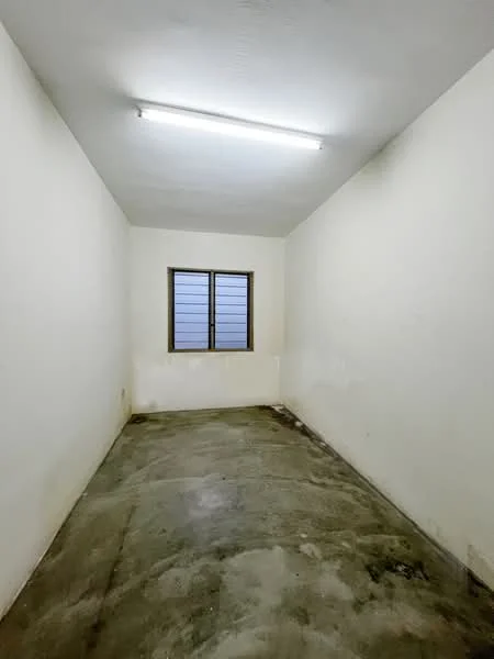 Room features: white painted walls, concrete flooring, single window with metal grille, fluorescent ceiling light.