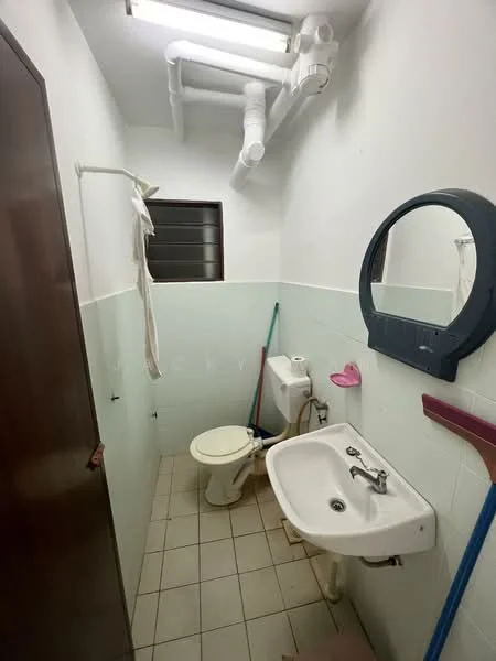 Bathroom features: white tiled walls, light green tiled walls, white ceramic toilet, white sink, round mirror, floor tiles, exposed plumbing, window, cleaning supplies, broom, mop.
