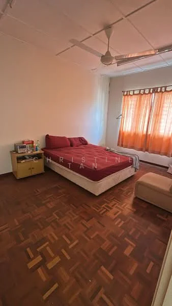 Bedroom features: queen-size bed with red bedding, wooden bedside table, lampshade, wooden flooring, ceiling fan, curtains with orange and brown tones, natural light from window, decorative wall with no visible artwork.