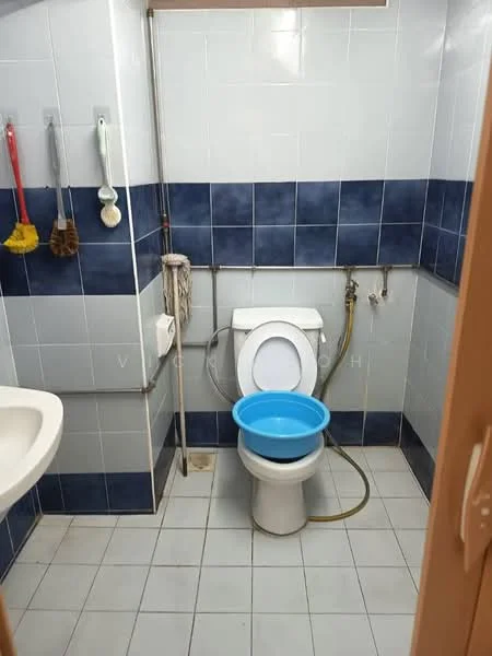 Bathroom features: white toilet, blue basin with chrome faucet, blue tiled walls, white tiled flooring, shower hose, cleaning tools on wall hooks, mop, bucket, chrome pipe fittings, wall-mounted mirror.