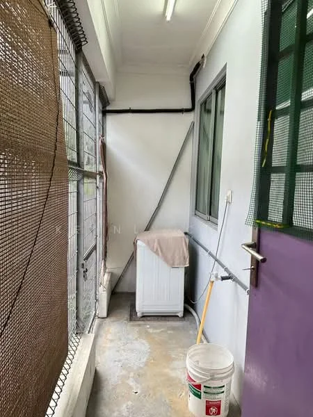 Laundry features: washing machine, concrete flooring, white walls, window with metal grille, purple door, cleaning supplies, bucket, broom, exposed pipes, light fixture.