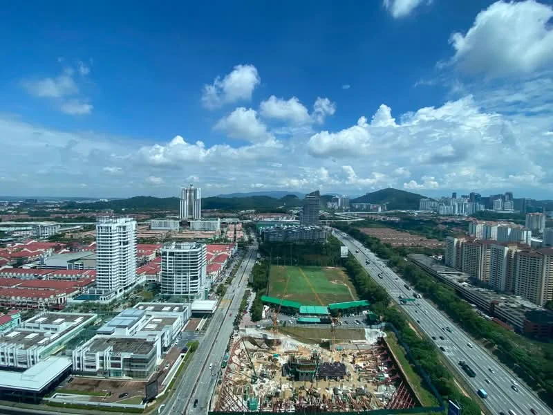 Exterior type: high-rise condominium; features: city skyline view, surrounded by greenery, highway visible, construction site in foreground, mixed-use development, urban landscape, multiple high-rise buildings, residential areas in background; style: modern.