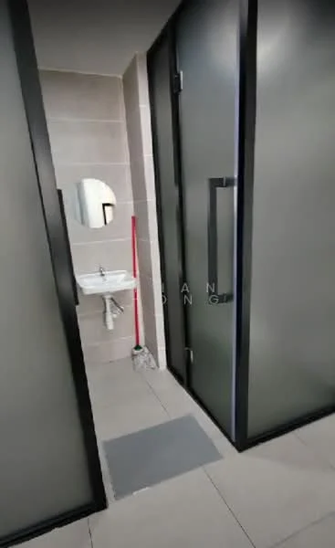 Bathroom features: grey tiled flooring, light grey wall tiles, white pedestal sink, round mirror, glass shower enclosure, sliding glass door, red cleaning mop, grey bath mat; style: modern.