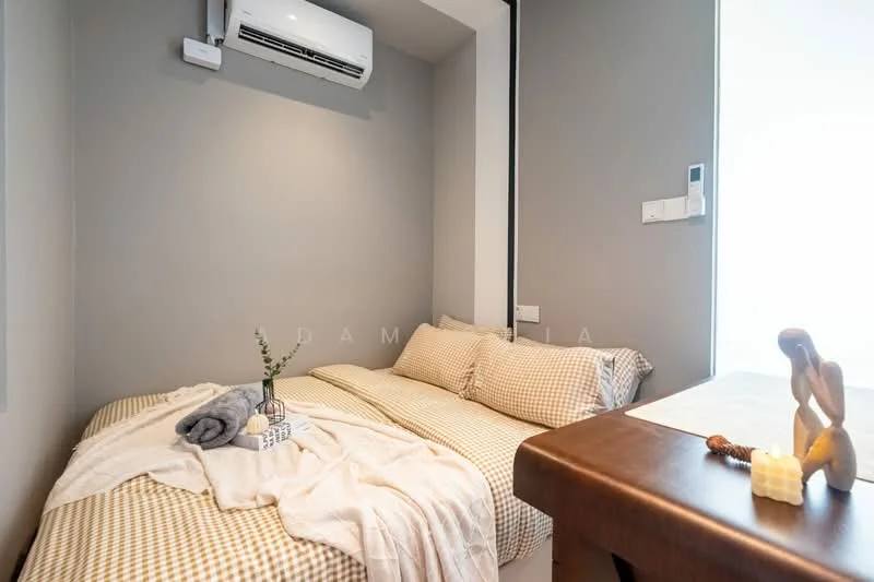 Bedroom features: queen-size bed with checkered bedding, wooden bedside table, decorative wooden figure, small potted plant, towels, wall-mounted air conditioning unit, grey painted walls, window with natural light; style: modern.