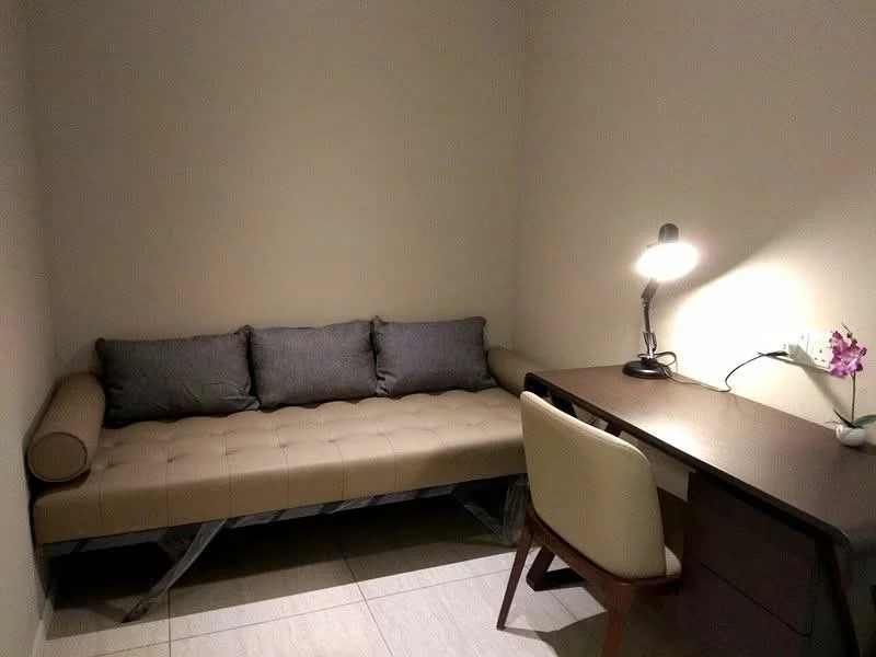 Study features: beige painted walls, tile flooring, tan upholstered bench with cushions, wooden desk, white upholstered chair, desk lamp, decorative plant, power outlet on wall; style: modern.