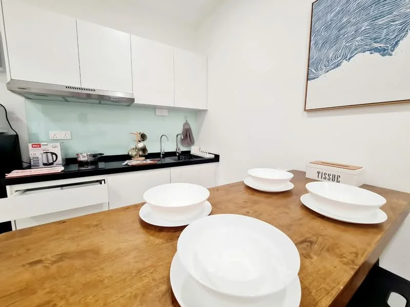 Kitchen features: white cabinetry, black countertop, stainless-steel sink, chrome pull-down faucet, glass backsplash, built-in oven, electric kettle, microwave, dining table with wooden surface, white dinner plates, decorative tissue box; style: modern.