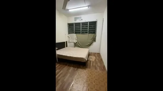 Bedroom features: wooden flooring, white painted walls, single bed, window with louvered shutters, ceiling fan, bedside rug, blanket on bed, curtain draped over window.