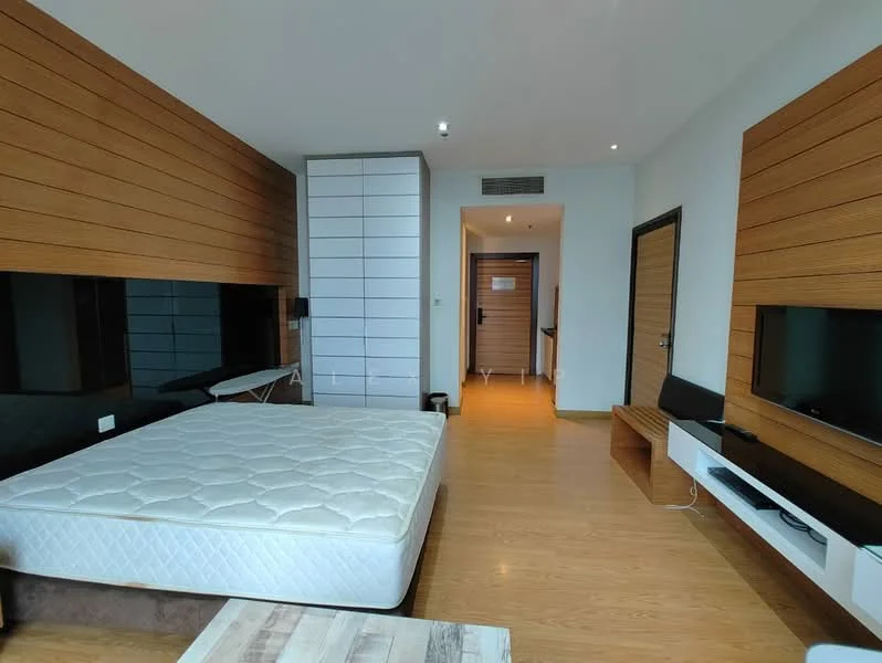 Room features: wood paneling on walls, light wood flooring, queen-size bed frame without mattress, built-in wardrobe with sliding doors, wall-mounted TV, TV console, recessed ceiling lights, open doorway leading to hallway, folding ironing board, wooden bench, neutral color scheme; style: modern.