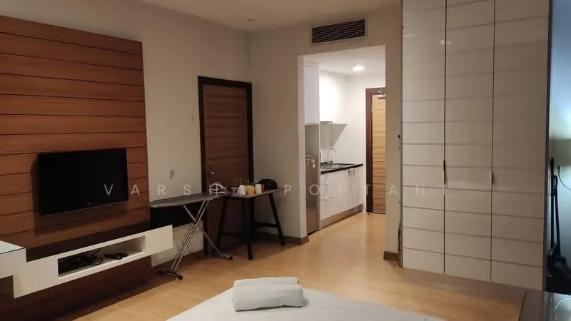 Room features: wood panel accent wall, flat-screen TV mounted on wall, white cabinetry, kitchenette with sink, stainless-steel appliances, wooden flooring, table with chairs, door leading to another room, light-colored walls, recessed lighting; style: modern.