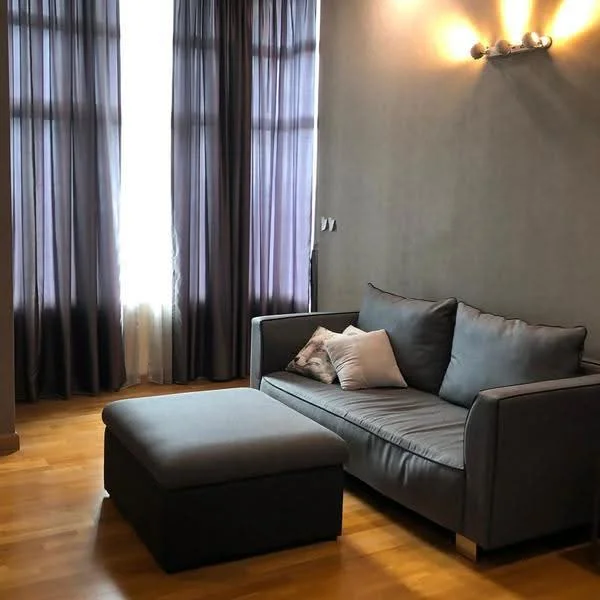 Living features: grey fabric sofa, ottoman, wooden flooring, floor-to-ceiling windows, sheer curtains, dark grey accent wall, wall-mounted light fixtures; style: modern.