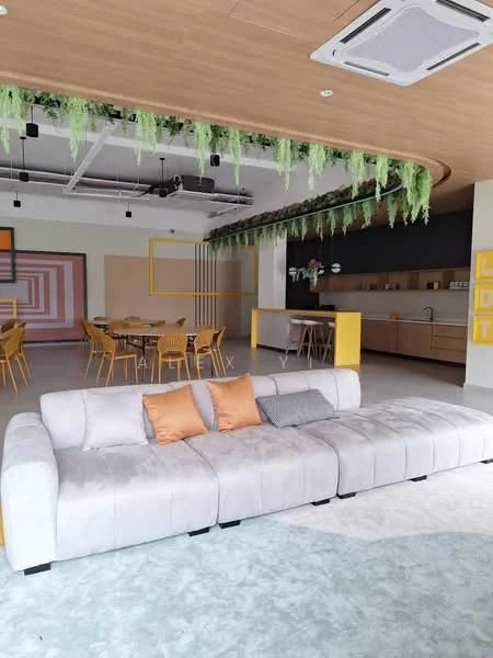 Living features: L-shape sectional sofa in light grey, two decorative cushions in orange, ceiling with wooden paneling, exposed ductwork, recessed downlights, hanging greenery, open-plan layout, light grey flooring, large dining area in background, kitchen area with cabinetry visible; style: modern.