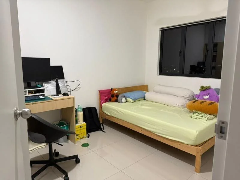 Bedroom features: queen-size bed with light green bedding, wooden bed frame, two large pillows, stuffed toys on bed, desk with computer monitor, keyboard and mouse on desk, wooden desk with drawers, black office chair, white painted walls, floor-to-ceiling window, tile flooring, backpack on the floor, bottle of water on the floor; style: minimalist; view: city.