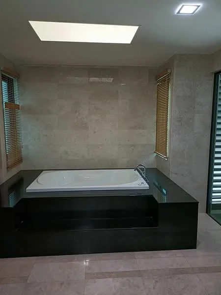 Bathroom features: freestanding bathtub, black stone platform, tile flooring, skylight, window with wooden blinds, neutral stone wall cladding, recessed ceiling lights; style: modern.