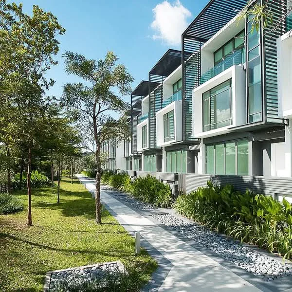 Exterior type: linked terrace house; features: modern facade with large windows, green landscaping with grass and shrubs, stone-paved walkway, trees providing shade, horizontal louvre screens, multiple storeys, contemporary architectural design, clear blue sky, well-maintained garden area; style: modern.