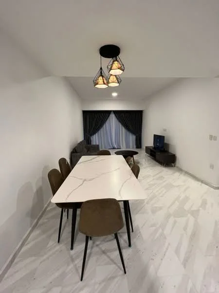 Dining features: 6-seater dining table with marble top, upholstered dining chairs in beige, pendant light fixture with three bulbs, white painted walls, light-colored marble flooring, floor-to-ceiling windows with sheer curtains, dark curtains, TV console, wall-mounted TV, sofa in grey fabric; style: modern.